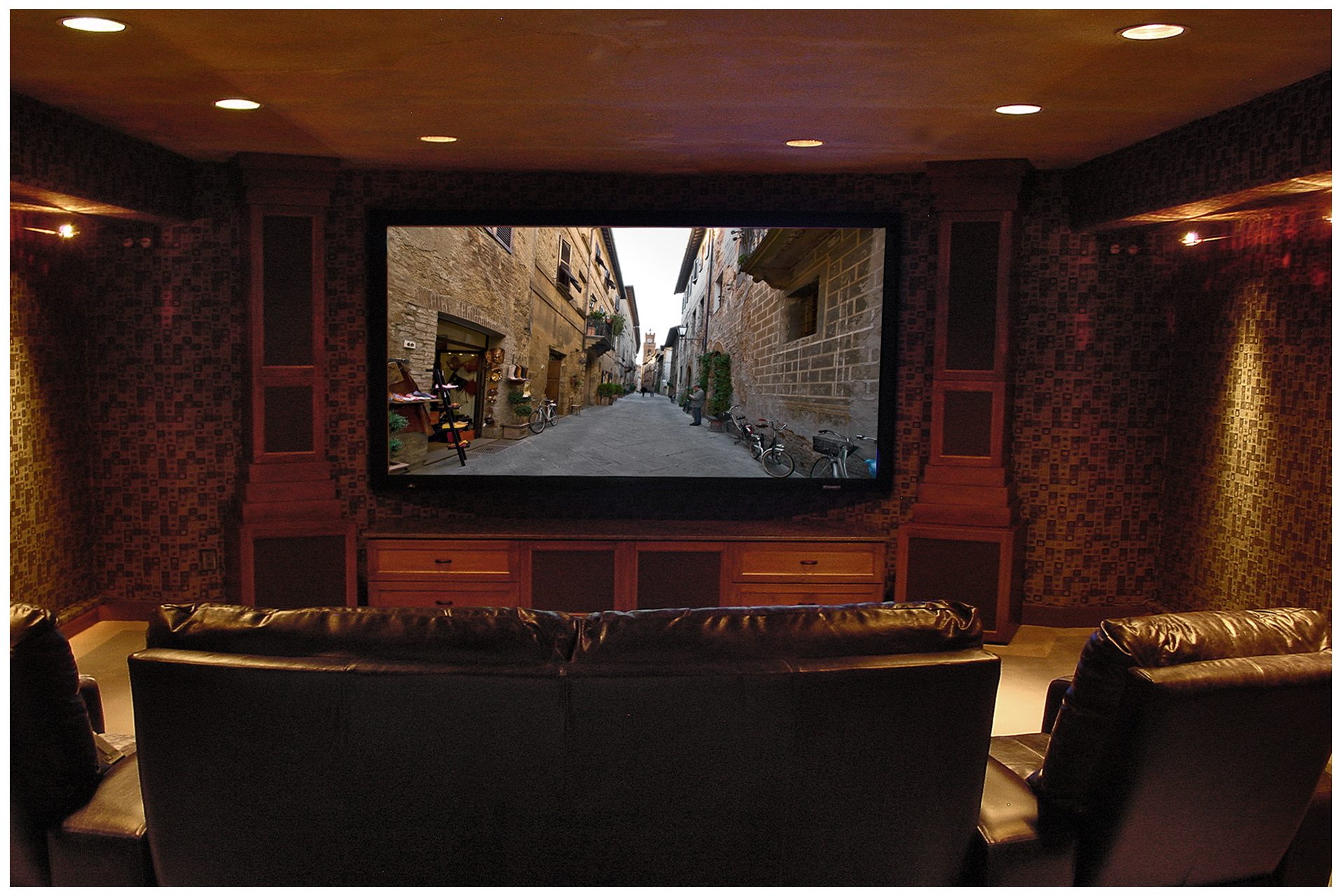 SMALL THEATER IN A DEDICATED ROOMCabinet towers flanking the screen enclosed all front subwoofers and main speakers.  A fixed projector above & behind seating area remained fairly invisible; side speakers were recessed into concrete basement walls flanking the viewing area, and a second pair of in-ceiling surrounds was recessed behind the viewing area. All electronics were placed in a closet space in an adjacent room.