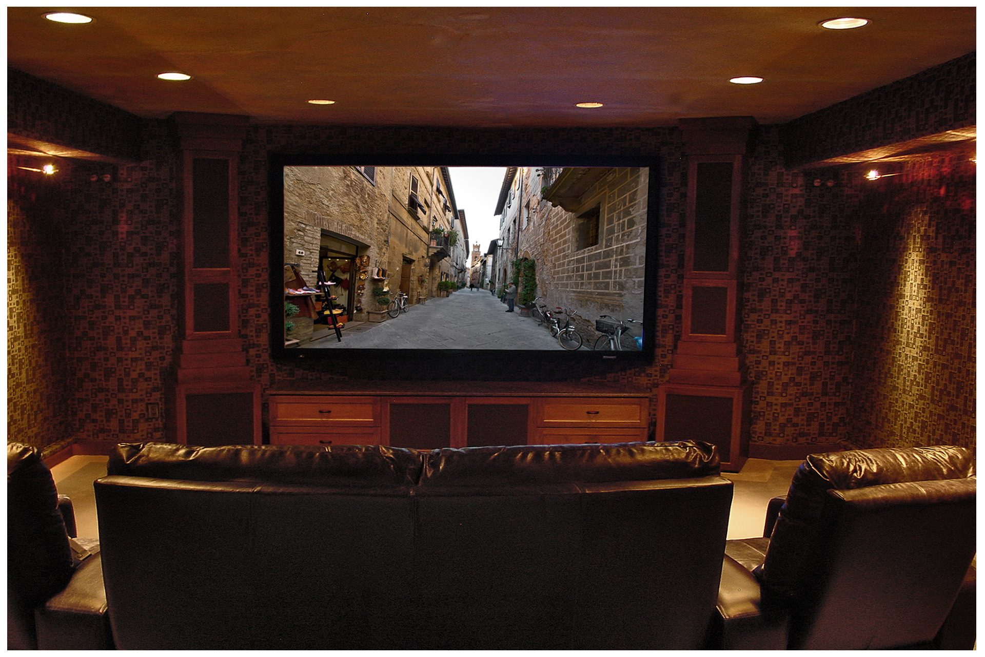 SMALL THEATER IN A DEDICATED ROOMCabinet towers flanking the screen enclosed all front subwoofers and main speakers.  A fixed projector above & behind seating area remained fairly invisible; side speakers were recessed into concrete basement walls flanking the viewing area, and a second pair of in-ceiling surrounds was recessed behind the viewing area. All electronics were placed in a closet space in an adjacent room.